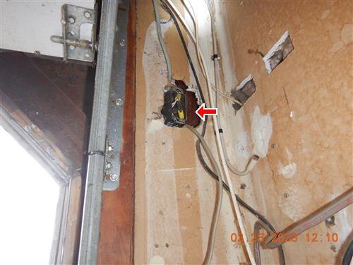 Uncovered electrical box beside a garage door frame, marked by a red arrow.